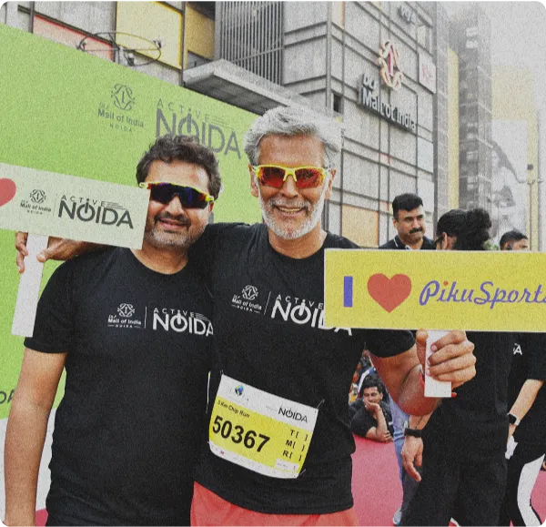 Indian actor and model Milind Soman holding a banner reading 'I Love Piku Sports' with another person.