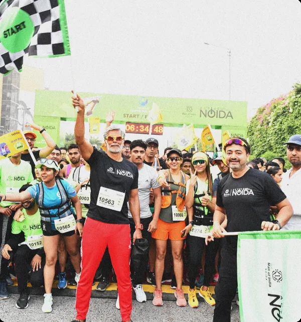 Milind Soman holding a flag, standing in front of a large crowd gathered to start a marathon. 